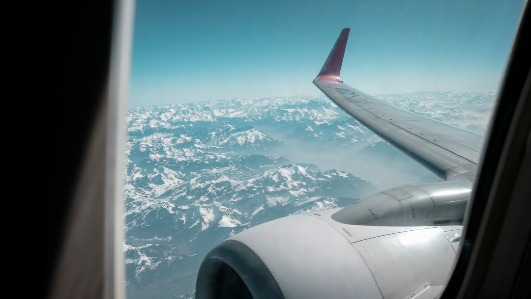 An airplane wing and engine seen from a passenger window above mountains