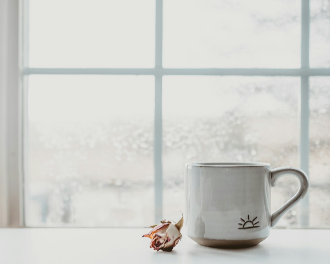 A coffee mug with a small sunrise design on a sunlit windowsill in the morning