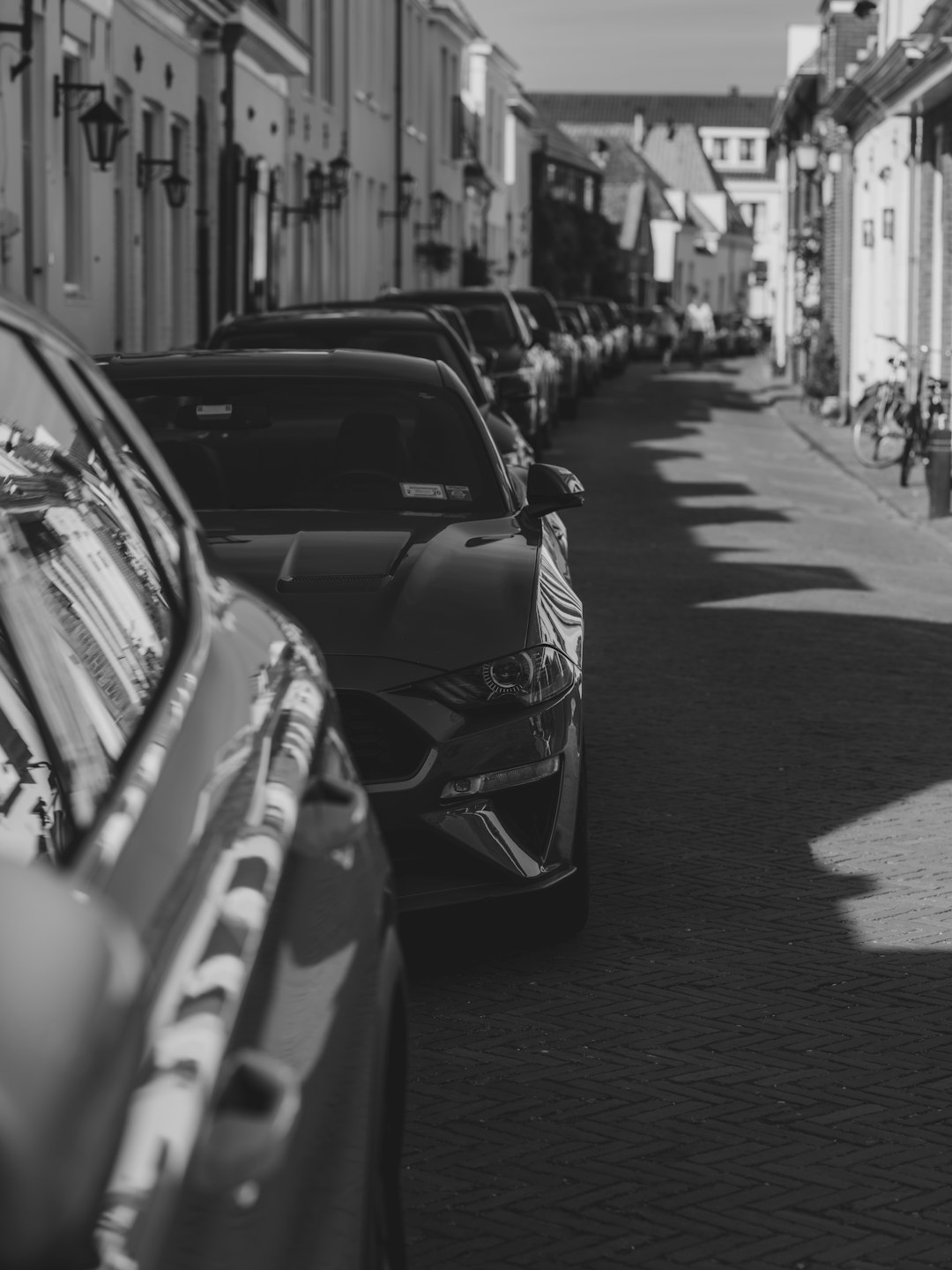 A row of cars parked along a narrow street in black and white