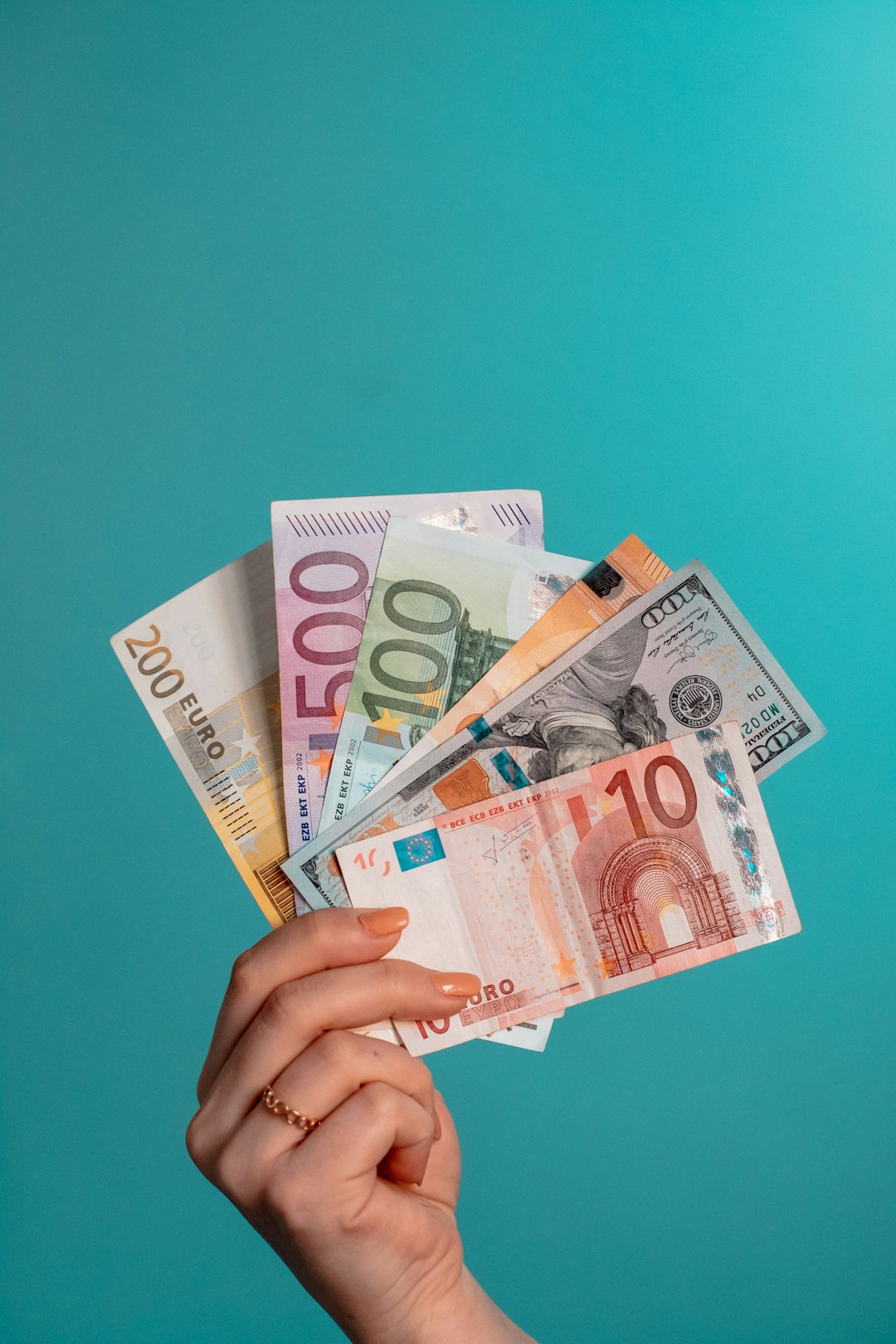 A hand holding a fan of euro and US dollar banknotes
