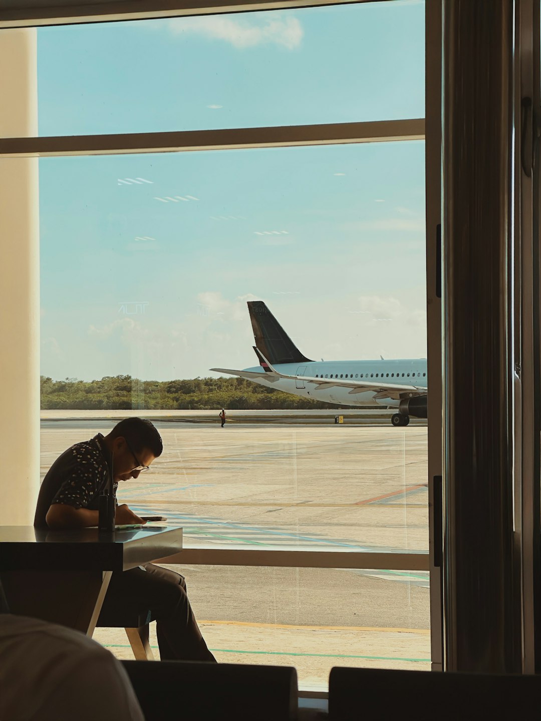 A seated passenger checking a phone beside an airport window