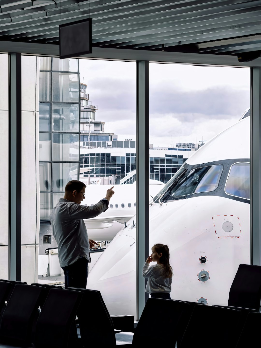 A father and child looking at planes from an airport gate window