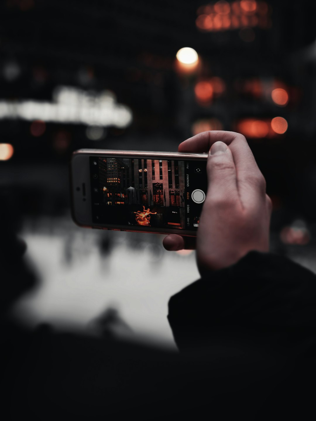 A hand holding an iPhone taking a photo in a city at night