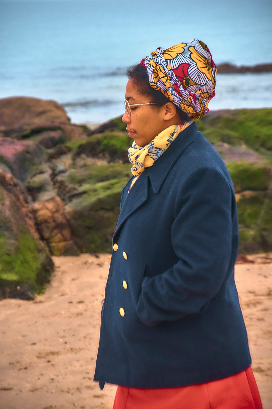 A woman in a headwrap walking along a sandy beach