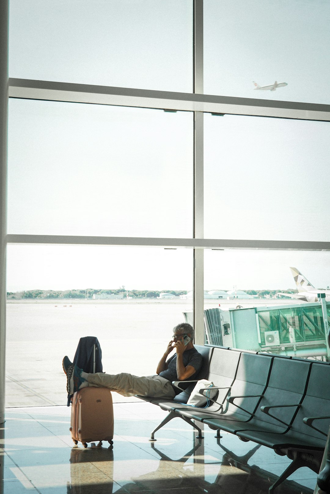 A man waiting at an airport gate with a suitcase and a plane outside